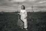 Une femme vêtue d'une longue robe blanche se tient dans un champ en tenant une bandura, un instrument folklorique ukrainien à cordes pincées.