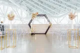Une installation pour une cérémonie de mariage avec des chaises transparentes et une arche décorée de fleurs.