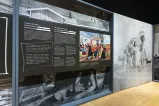 Un grand panneau d’exposition sur la gauche présente les mots « Un conflit de valeurs : La colonisation au début du Canada » et une peinture colorée. Sur la droite, on peut voir une grande photographie en noir et blanc représentant des personnes défilant dans des maillots de bain féminins des années 1940.