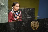 Une jeune fille autochtone porte une tenue traditionnelle et des boucles d'oreilles perlées, et ses cheveux sont tressés. Elle s'exprime à une tribune arborant le logo des Nations Unies.