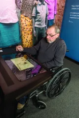 Un homme d'un certain âge est assis dans un fauteuil roulant devant un comptoir équipé d'un grand écran tactile.