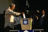 Un Nelson Mandela âgé sourit en tendant le bras droit pour déposer son bulletin de vote dans une grande boîte de scrutin en métal.