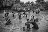 Un groupe de femmes et d’enfants rohingyas marchent dans un canal où l’eau est de deux à trois pieds de profondeur, en transportant leurs effets personnels.