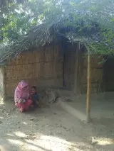 Une femme rohingya accroupie à côté d’un petit garçon devant une structure de bambou.