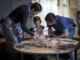 Une femme et un homme se penchent au-dessus d'une table où un jeune enfant joue avec une pile de photographies.