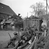 Un groupe de soldats armés regarde passer un char d’assaut.