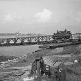 Un véhicule blindé traversant un pont temporaire qui enjambe un plan d’eau.