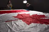 Deux femmes portant des gants et des tabliers de protection autour d’un grand drapeau du Canada, posé à plat sur une table.