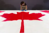 Une femme portant des gants de protection et un tablier prend des notes derrière un drapeau du Canada, posé à plat sur une table à l’avant-plan.