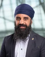 Un homme d'origine indienne, souriant, portant un dastar bleu foncé et un blazer gris.