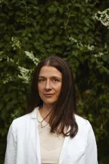 Headshot of a woman with long brown hair. She is wearing a white shirt.