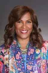 Une femme aux cheveux noirs, aux yeux sombres, sourit avec un haut multicolore.