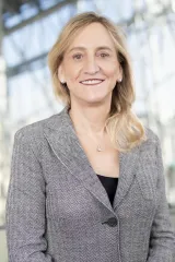 Une femme blanche aux cheveux et aux yeux châtain clair sourit à la caméra.