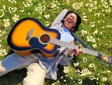 Kris Cahatol est en position allongée sur de l’herbe verte et rit. Des fleurs et des cœurs dessinés par ordinateur l’entourent. Kris tient une guitare sur sa poitrine.