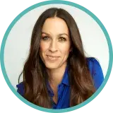 Une femme d’âge moyen aux longs cheveux foncés porte un chemisier bleu.