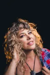 Une femme aux cheveux blonds et bouclés regarde la caméra avec un air coquet..