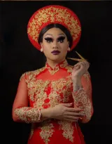 Une artiste de drag porte des vêtements culturels vietnamiens avec une coiffe et une robe longue rouge et or assorties.