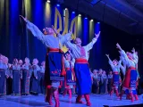 Un ensemble d’artistes d’Ukraine dansent sur scène; les personnes à l’avant regardent et tendent les bras vers le haut.
