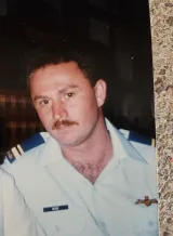 Un jeune homme en uniforme militaire blanc avec des épaulettes bleues sur l’épaule regarde sérieusement devant lui.