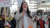 Une femme tenant un microphone relié à un porte-voix lors d’une manifestation dans une rue de ville.