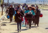Des familles portant des sacs marchent le long d’un chemin de terre.