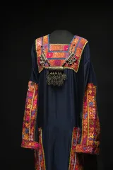 Un collier au motif complexe orne le cou d’une robe bleu foncé, dont les manches, la poitrine, les côtés et l’encolure sont décorés de motifs rouges, bleus et jaunes.
