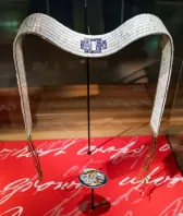 Une ceinture blanche et bleue faite de billes en coquillage est exposée sur un support.