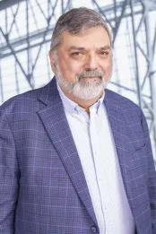 Un homme avec cheveux gris, porte un blazer bleu-mauve avec une chemise blanche.