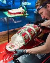Un homme qui porte des gants pose un tikinagan rouge et blanc dans une vitrine de musée.