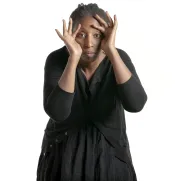 A woman peers at the camera through her hands, which are framed around her face.