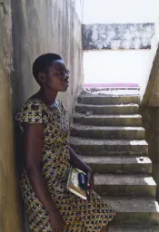 Une femme tenant un livre s'appuie contre un mur.