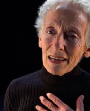 Une femme aux cheveux blancs et courts fait face à la caméra.