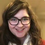 Femme blanche aux cheveux et aux yeux bruns, portant des lunettes rectangulaires foncées.