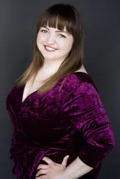 Renate Rossol, une femme aux cheveux et aux yeux bruns, affiche un large sourire. Elle porte une robe de cocktail d’un fuchsia éclatant.