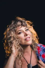 Une femme aux cheveux blonds et bouclés regarde la caméra avec un air coquet..