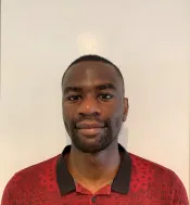 Une personne noire aux cheveux noirs très courts regarde la caméra avec un léger sourire. Elle porte une chemise rouge avec un motif imprimé représentant un dessin au trait noir et un col noir.