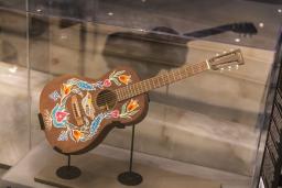 Une guitare peinte de motifs floraux est placée sur un support dans une vitrine.
