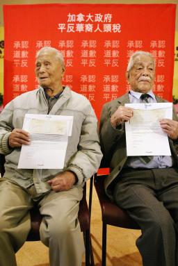 Deux hommes âgés assis, qui tiennent un document dans leurs mains.