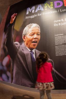 Une fillette regarde une grande photographie d'un homme qui a le poing en l'air, sur le panneau titre d'une exposition muséale.