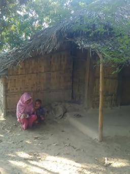 Une femme rohingya accroupie à côté d’un petit garçon devant une structure de bambou.