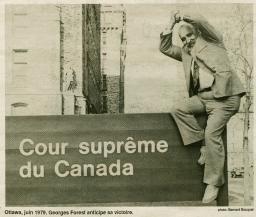 Un homme assis sur une pancarte portant l’inscription « Cour suprême du Canada » en français se tient les mains jointes au-dessus de la tête en symbole de victoire.
