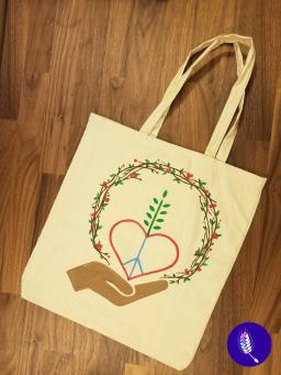 Canvas tote bag painted with designs including an open hand, a heart, a peace sign, a growing plant and a wreath.
