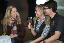 Trois personnes assises ensemble à une table dans un espace du Musée, buvant du vin.