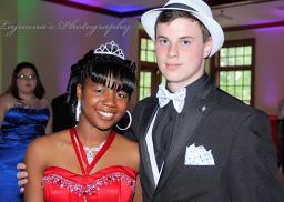Deux jeunes gens posent pour une photo tête et épaules. À gauche, une jeune femme noire porte une robe bustier rouge. À droite, un jeune homme blanc porte un smoking noir et un fedora blanc. 