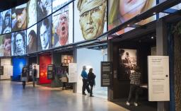 Des gens regardent une série d'expositions dans un musée. Il y a de grandes images dans une grille au-dessus.