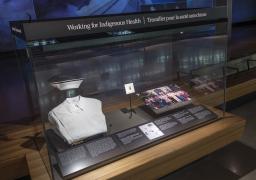 Une vitrine du Musée intitulée « Travailler pour la santé autochtone » et contenant l’uniforme et l’épinglette de diplômée d’une infirmière et une photo de groupe. 