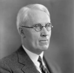 Portrait officiel d’un homme aux cheveux blancs portant des lunettes et un costume trois pièces.