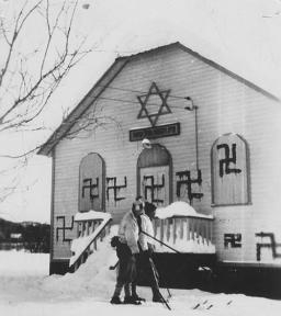 Deux personnes en skis devant une synagogue où plusieurs croix gammées ont été peintes, Sainte-Marguerite, Québec, 1938.