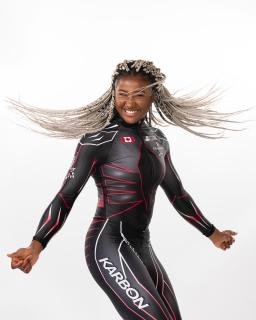Une femme noire portant un uniforme olympique de bobsleigh pose avec ses cheveux flottants dans l'air.