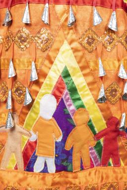 Cette section de la robe à clochettes orange montre deux figures humaines à l’intérieur d’un tipi multicolore. L’un des personnages porte une chemise orange.